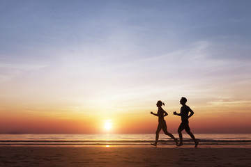 Silhouette of two runners running on the beach at sunset