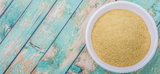 Dried bakers yeast in white bowl over wooden background