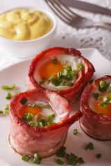 Fried eggs wrapped in bacon close-up on a plate and sauce. vertical

