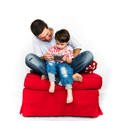 Father and son playing with smart phone together on a red sofa - isolated on white background
