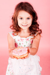 Smiling kid girl 5-6 year old holding glazed pink donut over pink. Looking at camera. Childhood. 