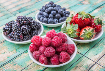 Blackberry, strawberry, blueberry and blackberry in white bowl over wooden background