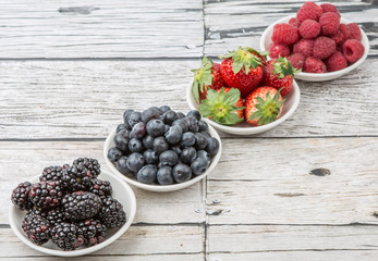 Blackberry, strawberry, blueberry and blackberry in white bowl over wooden background