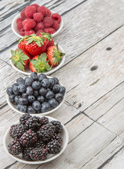 Blackberry, strawberry, blueberry and blackberry in white bowl over wooden background