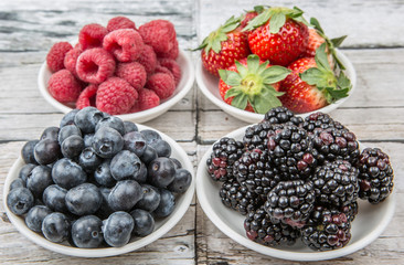 Blackberry, strawberry, blueberry and blackberry in white bowl over wooden background