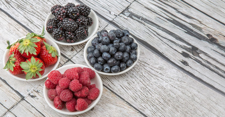 Blackberry, strawberry, blueberry and blackberry in white bowl over wooden background