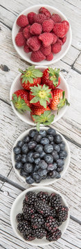 Blackberry, strawberry, blueberry and blackberry in white bowl over wooden background