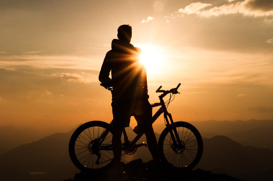 Mountainbiker am Gipfel mit seinem Fahrrad bei Sonnenuntergang