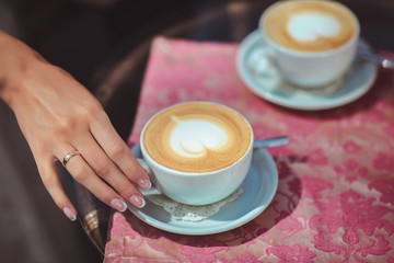 Two cups of hot cup of coffee, with heart shape on the table, latte art