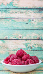 Raspberry fruit in white bowl over wooden background