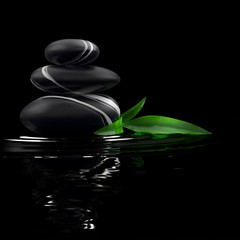 Spa stones and bamboo leaf in waters on black background.