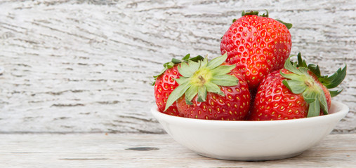 Strawberry fruits in white bowl over wooden background