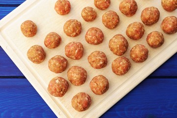 Raw homemade meatballs on white plastic cutting board
