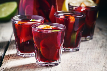 Sangria with fruit in a glass and a jug on old wooden background