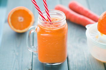 Healthy carrot orange smoothie in a jar with tube wooden background. 