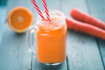 Healthy carrot orange smoothie in a jar with tube wooden background. 