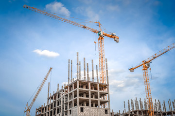 Fototapeta premium Modern houses under construction and industrial construction cranes