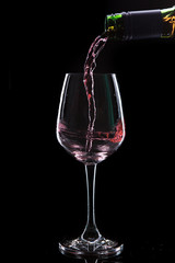 Red wine pouring into  wine glass. Isolated on black background