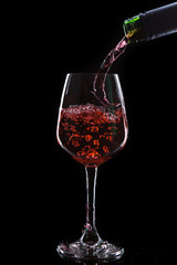Red wine pouring into  wine glass. Isolated on black background