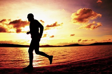 Silhouette of sport active man running and exercising on beach at vivid colorful sunset.