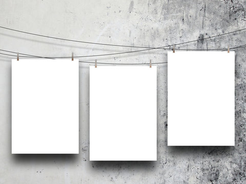 Close-up of three hanged paper sheet frames with pegs on concrete wall background