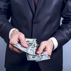 Man in a suit holds US dollars on grey background