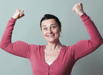 muscle concept - joyous beautiful 40s woman flexing her muscles up for metaphor of female success...