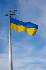 Waving blue-yellow Ukrainian flag with the emblem of Lviv at the height of the flagpole on the blue sky background. A vertical view. Lviv, Ukraine