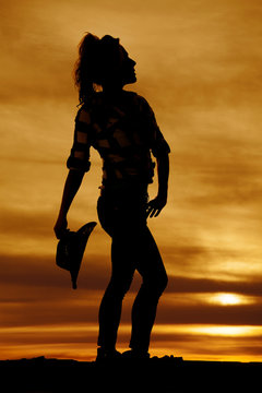 silhouette of a cowgirl holding her hat behind her looking up