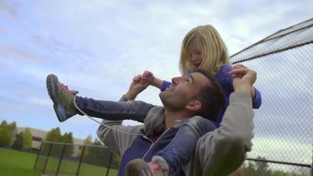 Father jumps up and down with his daughter on his shoulders and she has a blast