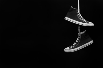 A pair of black and white sneakers hanging by their laces in front of a black background