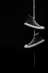 A pair of black and white sneakers hanging by their laces in front of a black background - 98986521