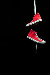 A red pair of sneakers hanging by their laces in front of a black background