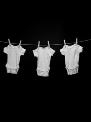 Black and white image of three baby onesies hanging on a clothesline in front of a black background