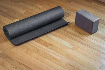 A black yoga mat rolled up next to a brown yoga mat on a wooden floor - 98986541
