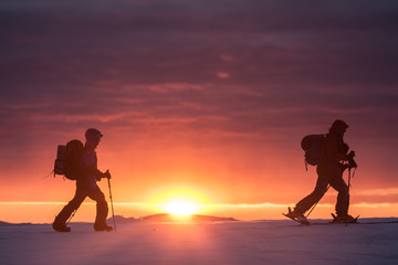 Two skiers walking mountains against sunset