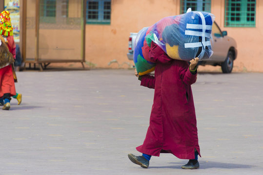 Man is carrying big bag with goods across the street in Marrakec