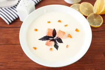 Delicious salmon cream soup in white plate on wooden table, close up