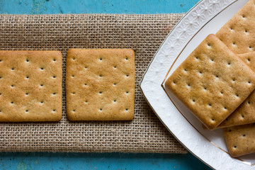 Square cracker biscuits on a linen napkin and a triangular portion of white ceramic plates with...