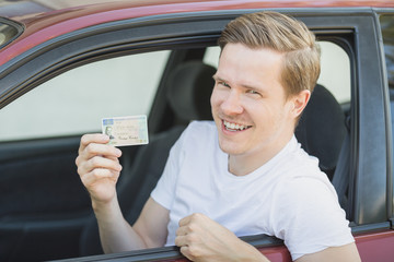 Junger Mann sitzt im Auto und zeigt seinen Führerschein