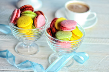 Sweet and colourful French macaroons in the dessert bowl near to a Cup of coffee on wooden table