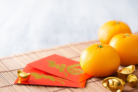 Chinese New Year - Mandarin Orange, Gold Sycee (Foreign Text Means Wealth) And Red Packet (Foreign Text Means Spring Season) On White Painted Wood Table