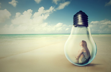 woman sitting inside a light bulb on a beach looking at the ocean view