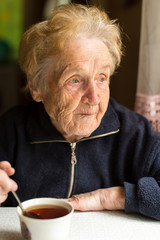 Old woman drinking tea near the window.