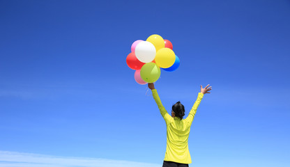 young cheering woman with colorful balloons on mountain peak