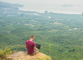 Fototapeta na wymiar Man working with laptop sitting on the rocky mountain on beautiful scenic clif background. Thailand. Krabi . 