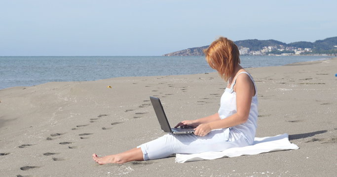 redheaded girl working at a laptop sitting on the beach