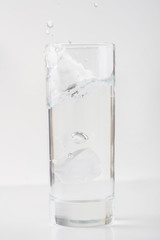 Glass of water with ice on white surface.