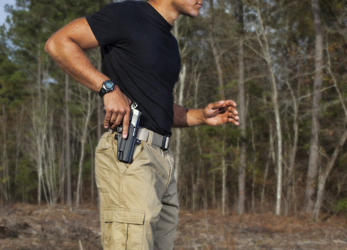 Drawing a handgun at the moment needed in a field surrounded by trees outdoors