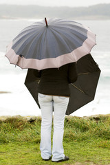 woman with two umbrellas in stormy day watching the sea
